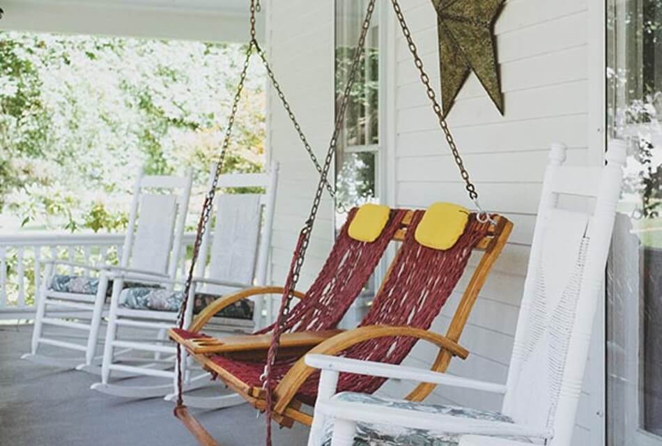 Three white rocking chairs and a two person hanging swing on an outdoor porch