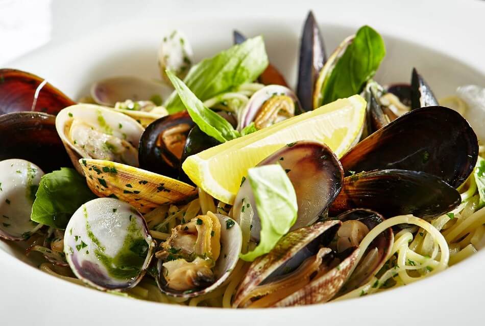 White bowl filled with open mussels over noodles with a lemon wedge