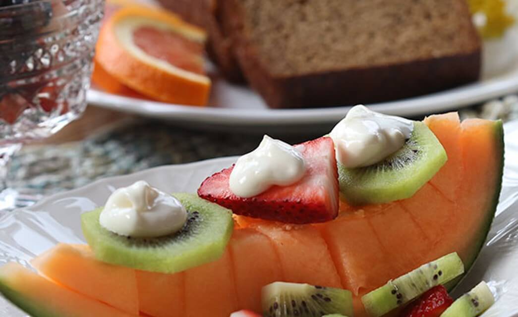 White plate with slice of cantelope melon and sliced kiwi and strawberries