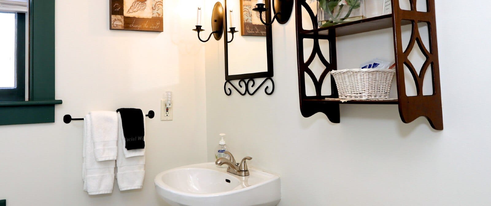 White bathroom with pedestal sink, black framed mirror, hanging towels and wood shelf