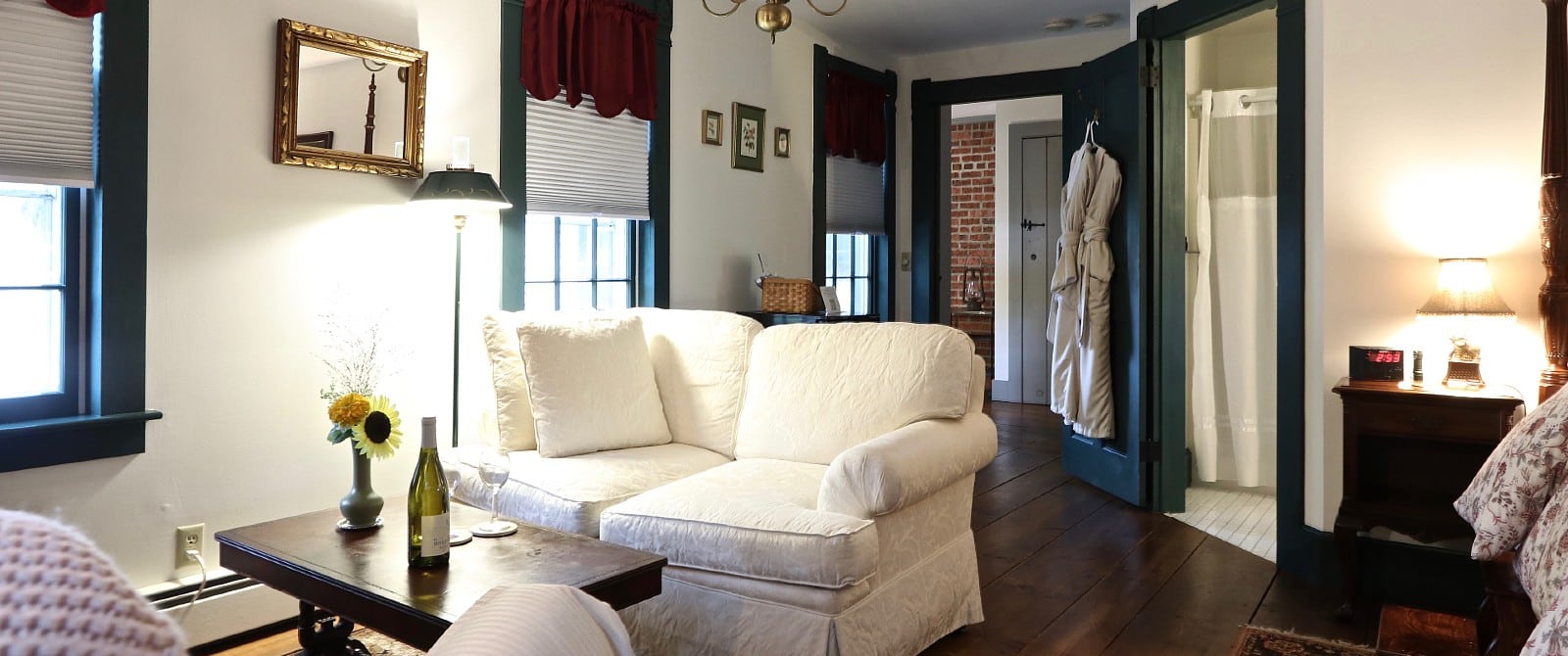 Sitting area of a bedroom with a white couch, coffee table and robe hanging on a doorway to a bathroom