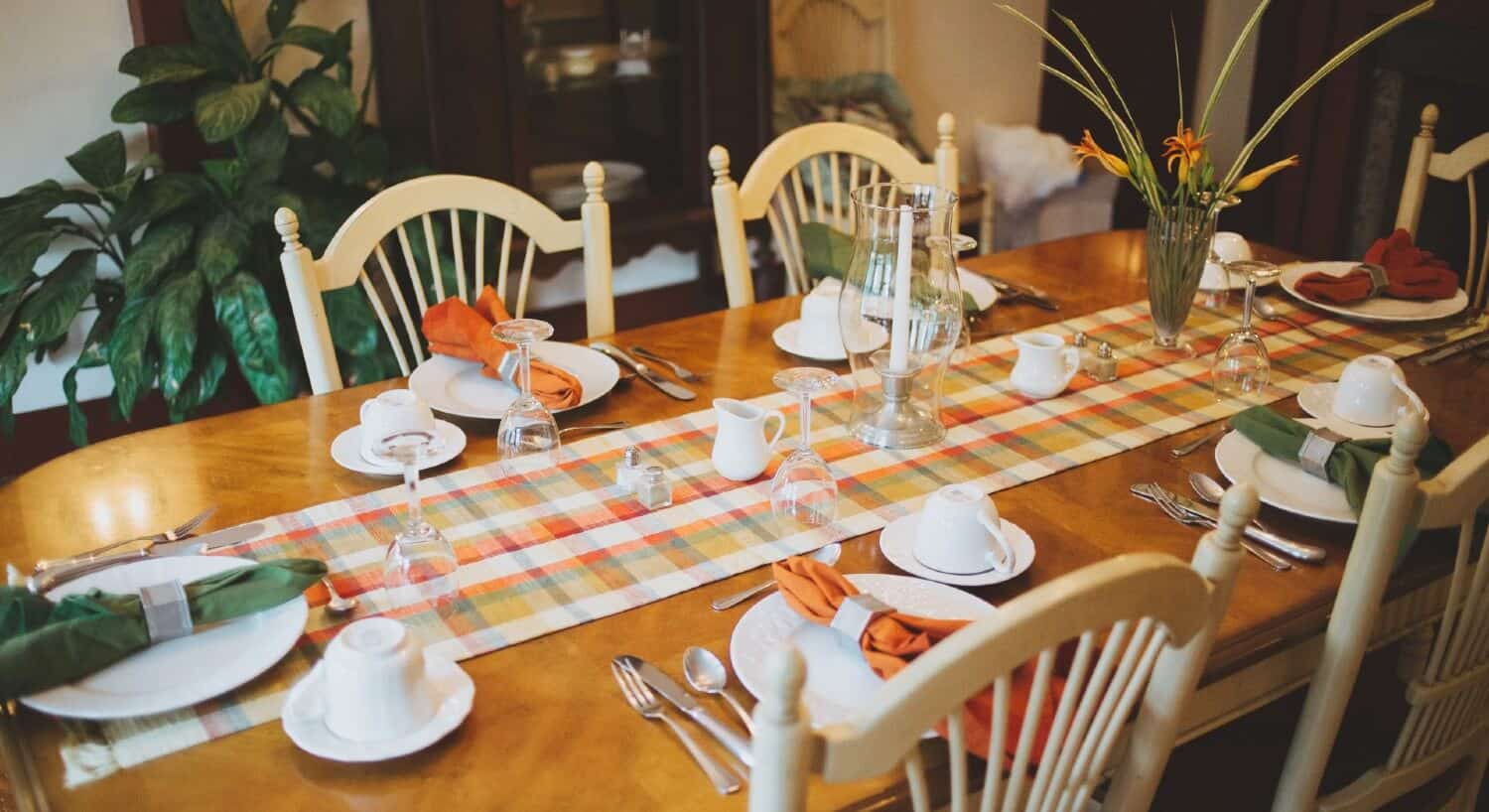 Brown dining table with white chairs with plaid runner and white place settings