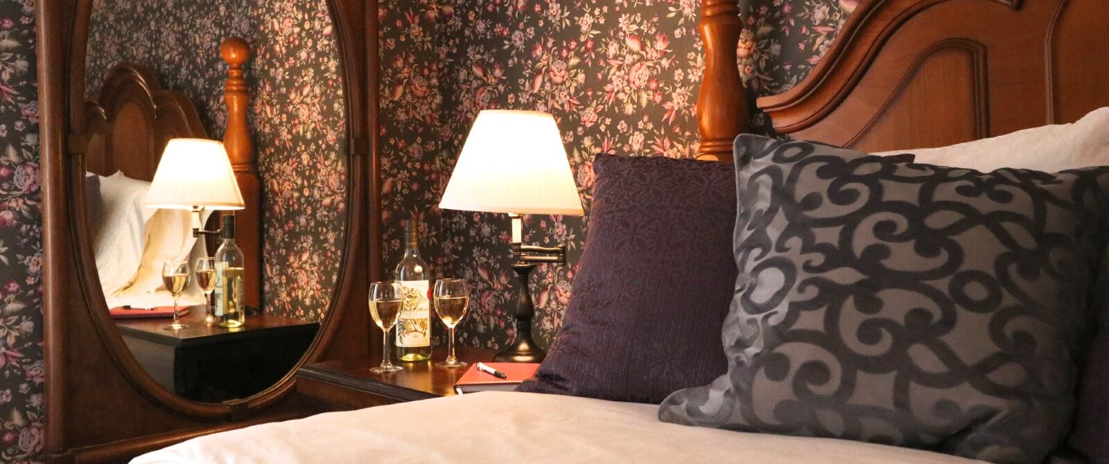Bedroom with floral wallpaper, queen bed, side table with two glasses and a bottle of white wine