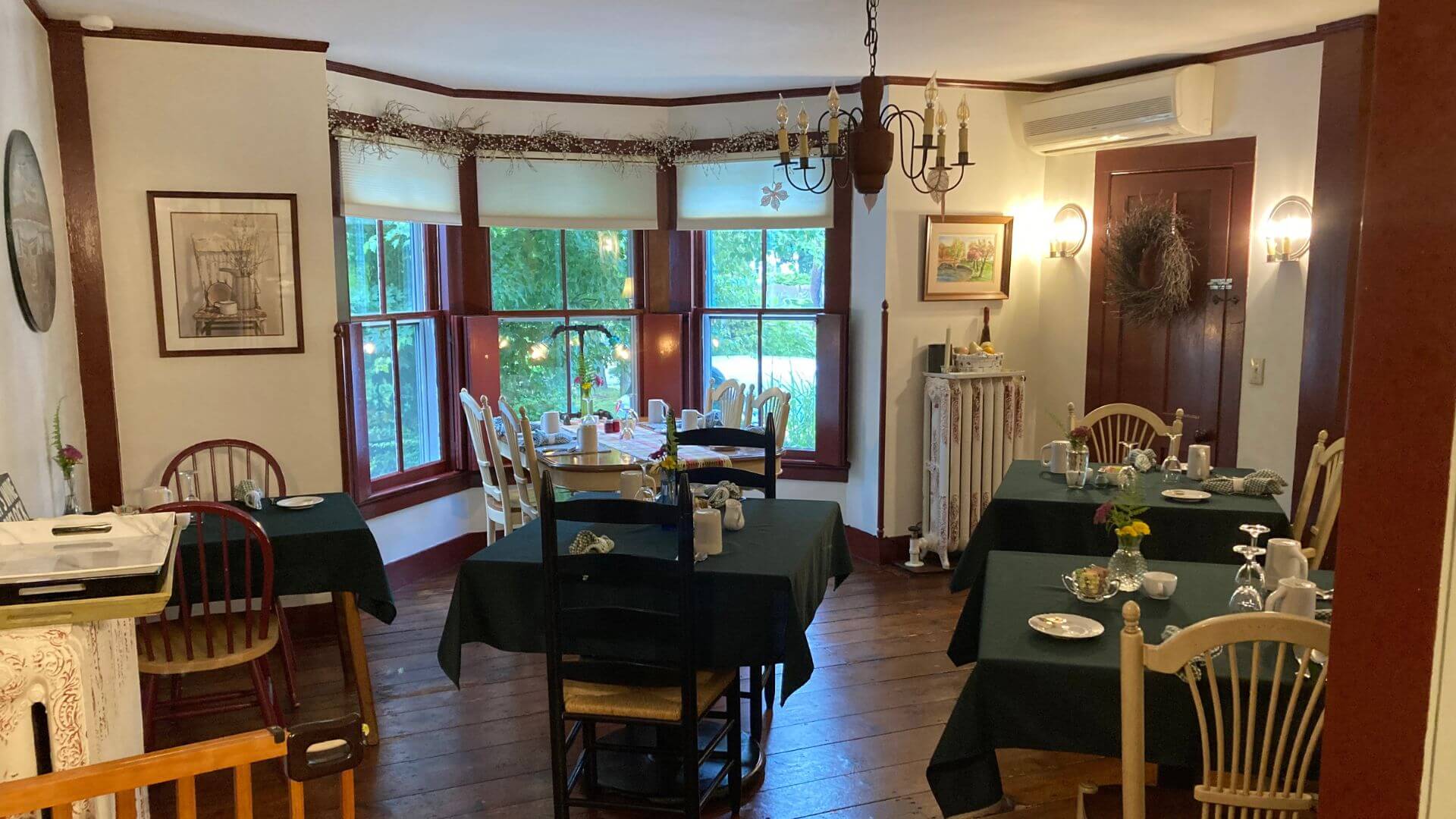 Breakfast room in a home with large bay window and five tables set with green tablecloths