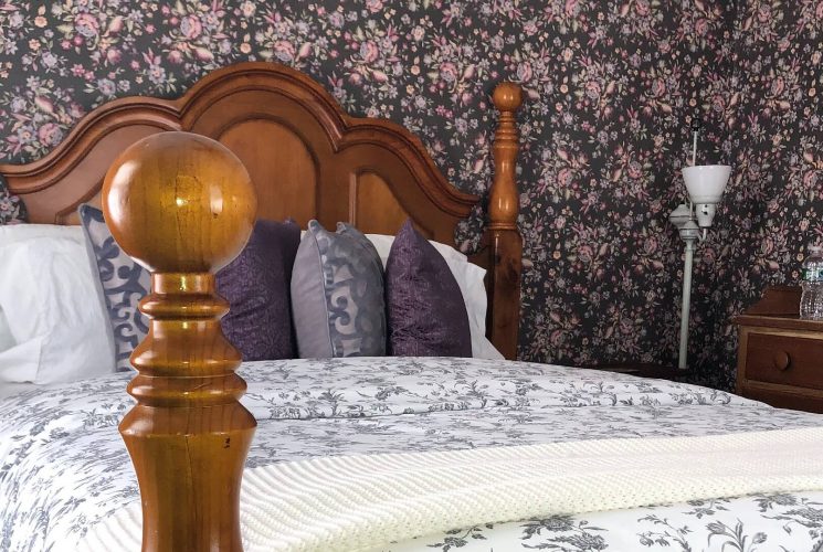 Bedroom with four poster queen bed, floral wallpaper and wood dresser