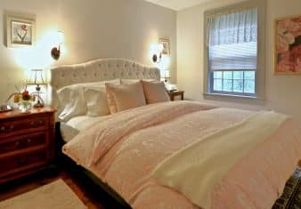 King bed with cream upholstered headboard in pretty bedroom with pink and floral accents