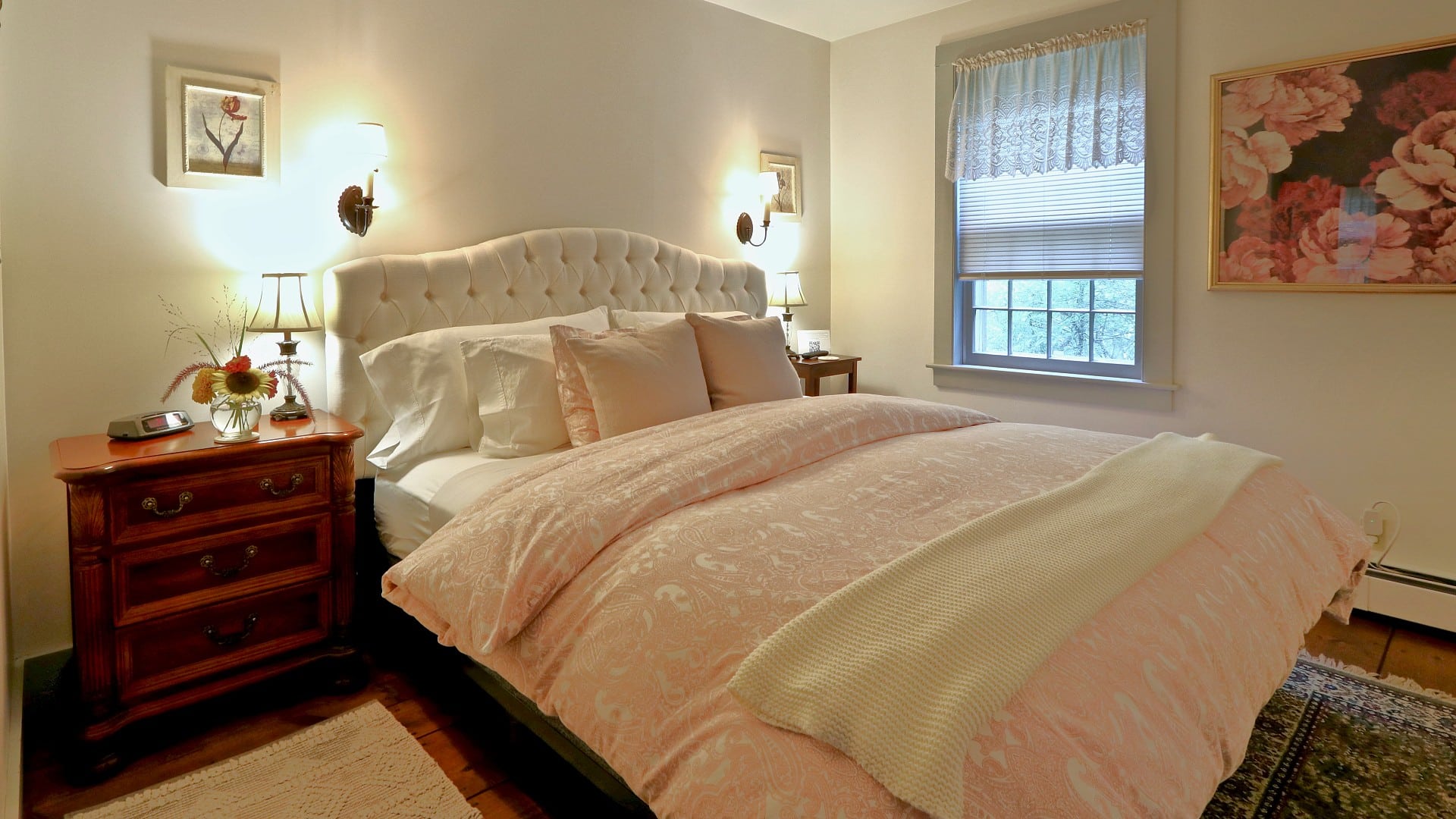 King bed with cream upholstered headboard in pretty bedroom with pink and floral accents