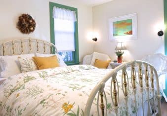 Bright and airy bedroom with queen bed, white floral bedding, wicker sitting chairs and windows