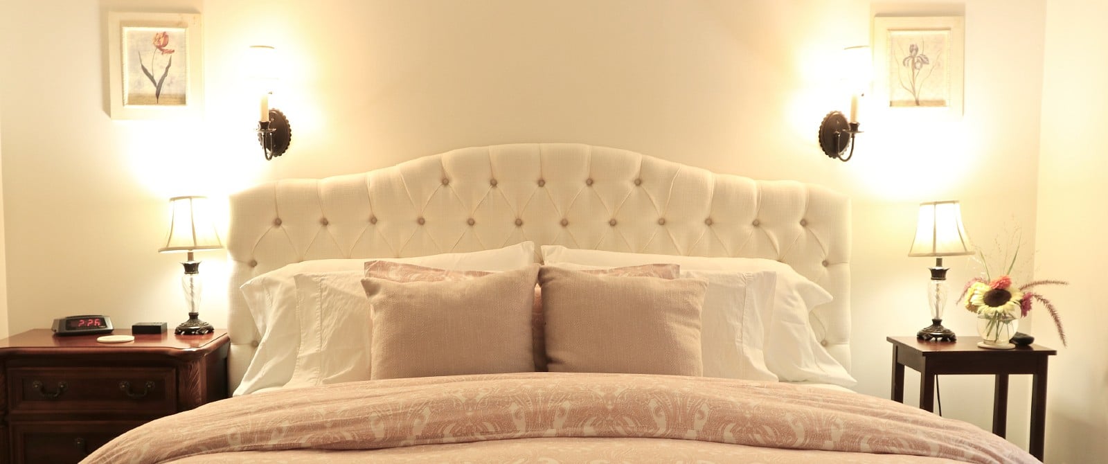King bed with white upholstered headboard, pink and white bedding and soft light lamps