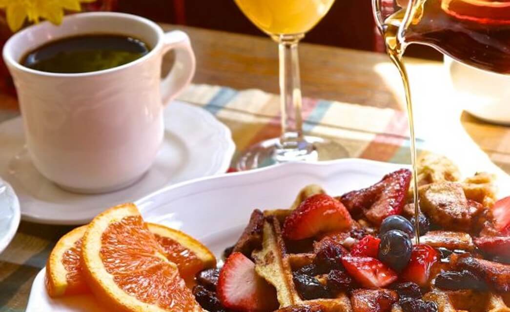 Breakfast plate with waffle, berries, sliced oranges next to cup of coffee and glass of orange juice