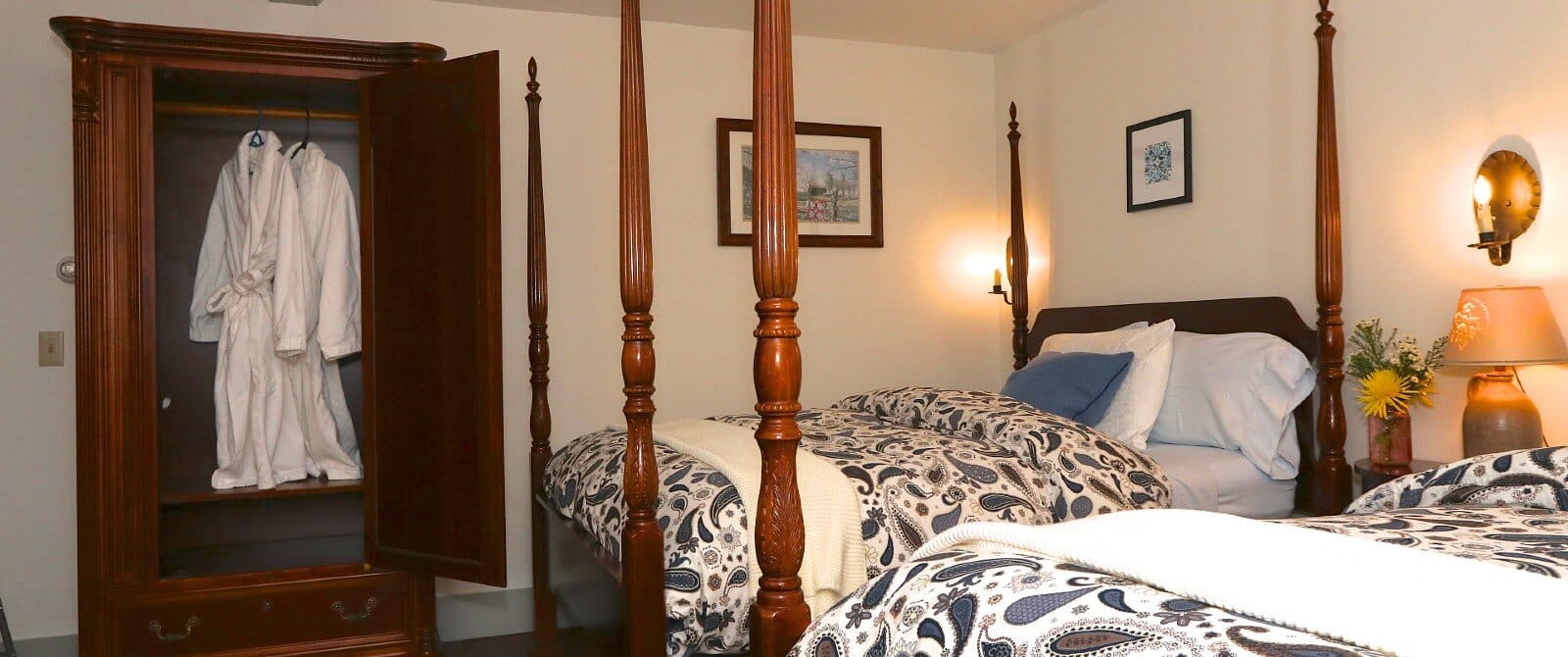 Two four poster double beds in bedroom with open armoire showing two white hanging robes