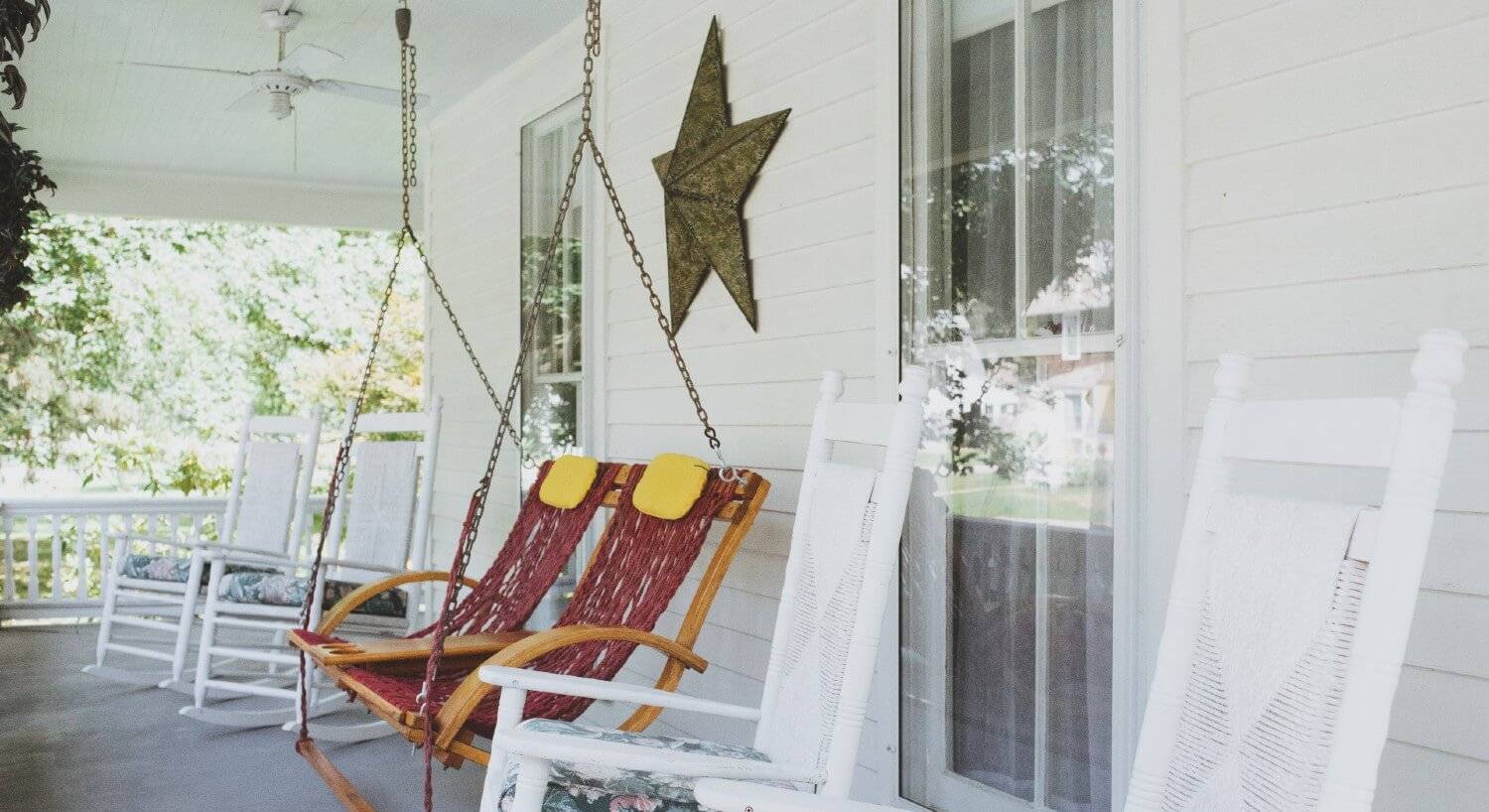 Outside porch with four white rocking chairs and hanging swing