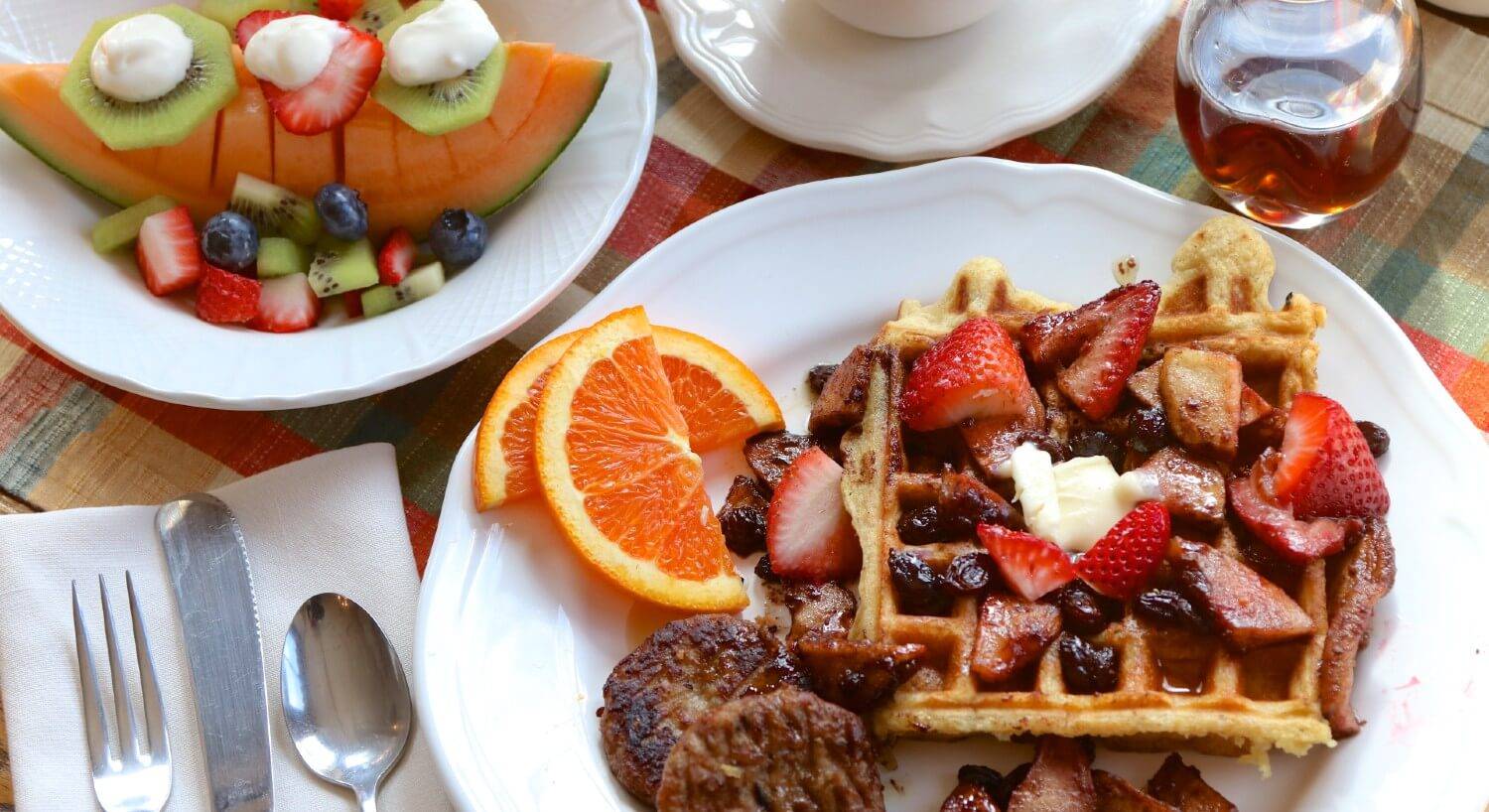 White plate with waffles covered in strawberries with sliced oranges and sausage patties