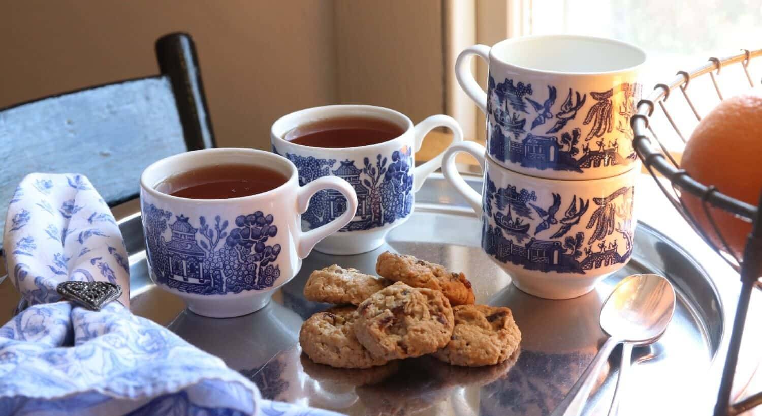 Silver tray with four blue and white mugs, two filled with tea and five cookies