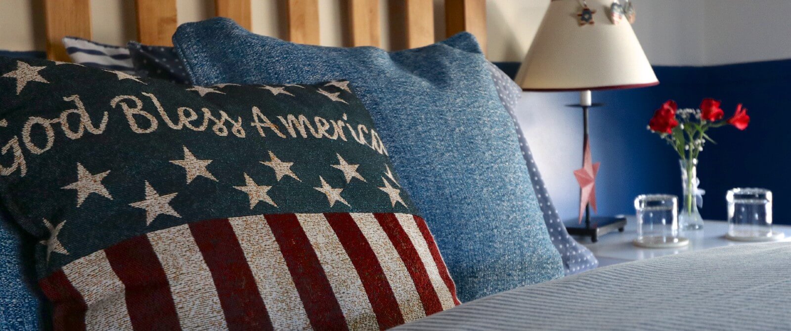 Bed with denim bedding, an American flag pillow and side table with lamps and water glasses