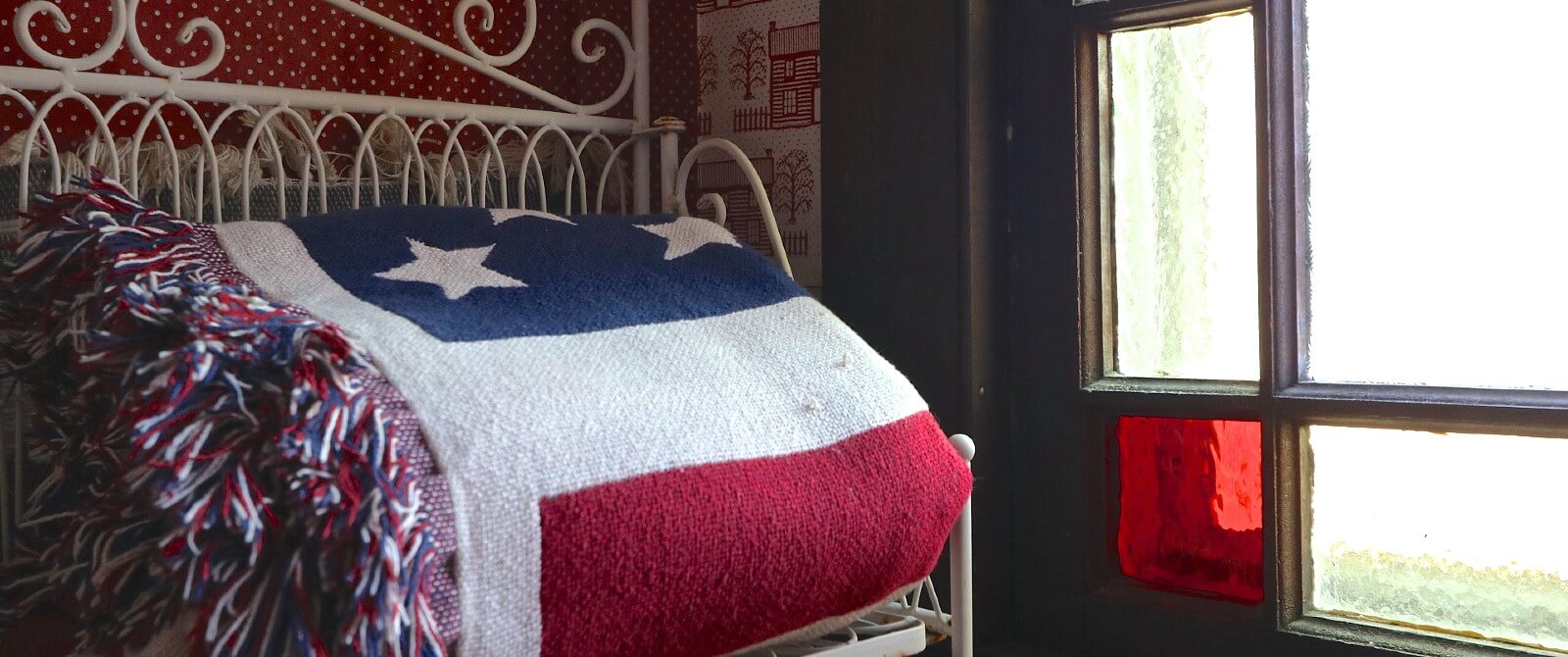 American flag blanket sitting on a white iron shelf next to a window