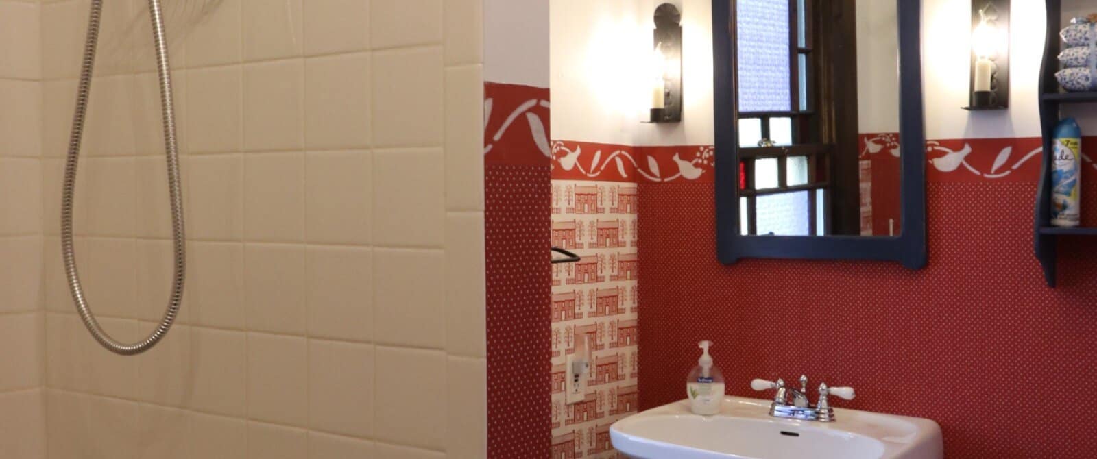 Bathroom with pedestal sink, blue framed mirror, red wallpaper and tiled shower