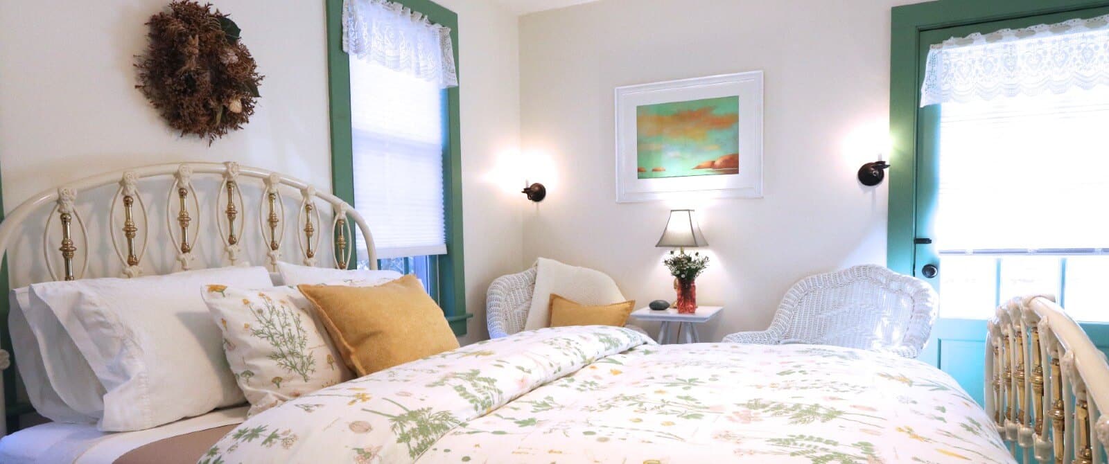 Bright bedroom with queen bed, floral bedding, white wicker chairs and green door