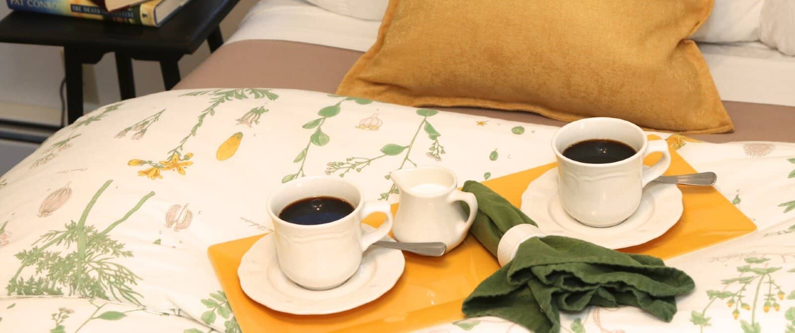 Yellow platter with two coffee cups with cream on a bed with floral quilt