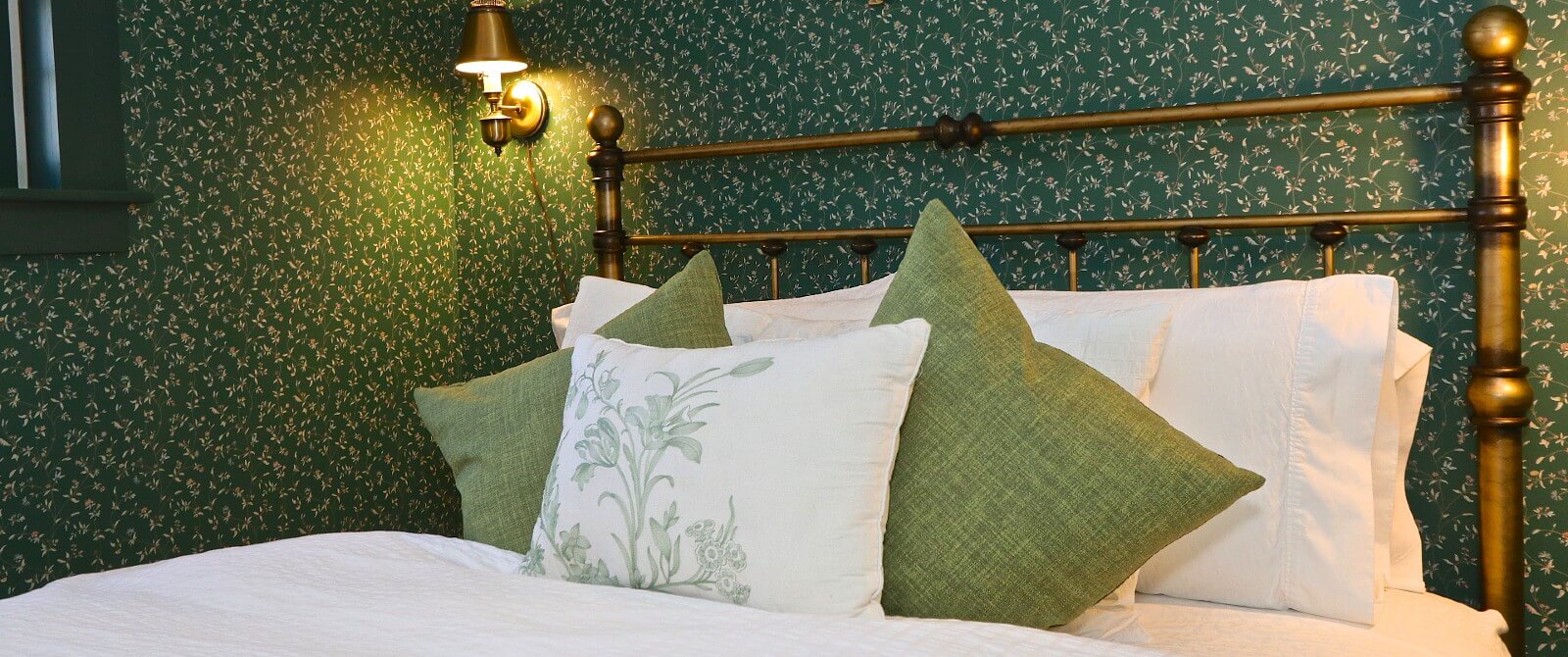 Bedroom with green floral wallpaper, wrought iron bed with white and green bedding and pillows